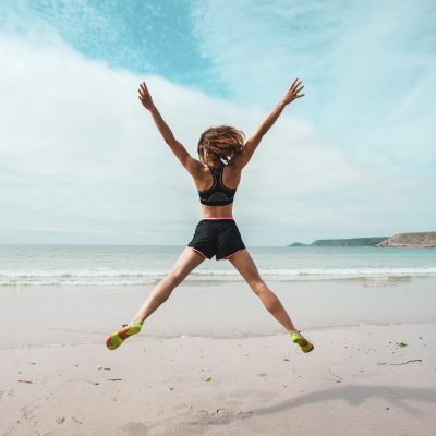 A young woman is doing star jumps on the beach by the sea