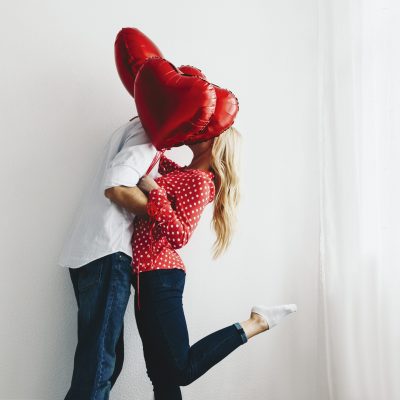 Couple. Love. Valentine's day. Emotions. Man and woman are kissing behind the red heart-shaped balloons